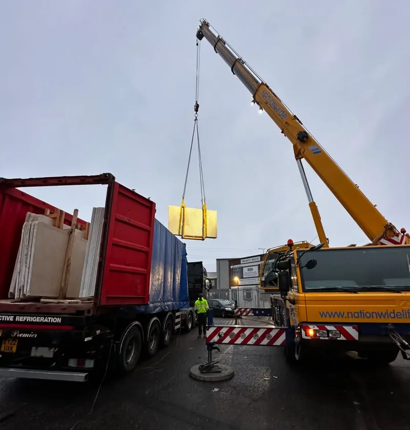 A crane lifting a pack of stone slabs from a container lorry